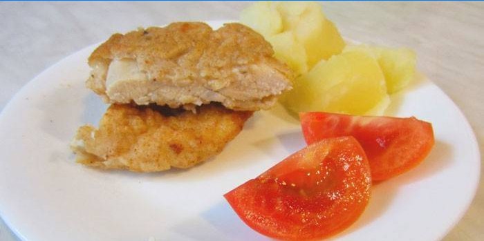 Hühnerkotelett im Teig mit Kartoffeln und Tomaten auf einem Teller